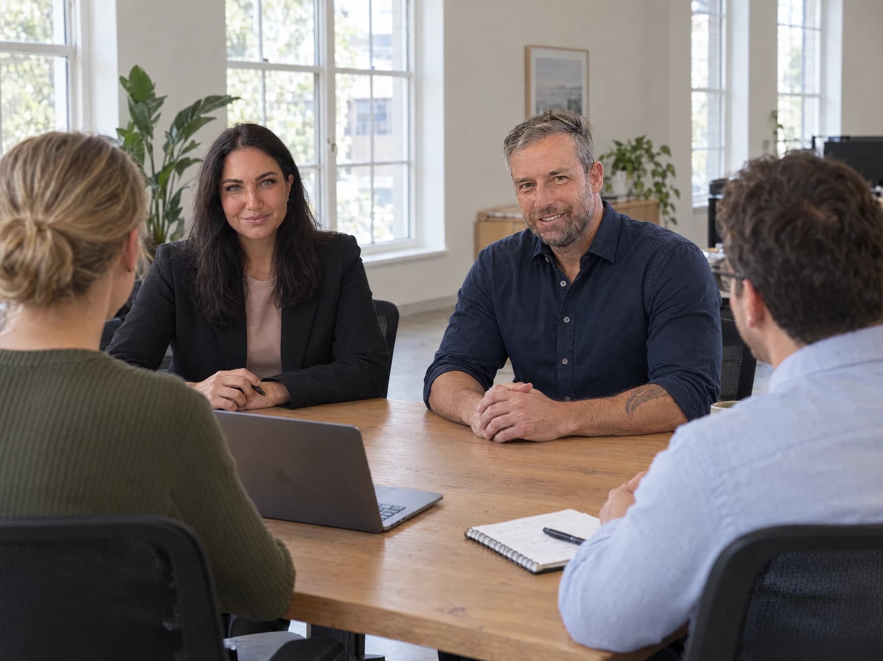 Illustrative office scene with Cayley Wright, Chris Bowler and colleagues discussing work around a meeting table.